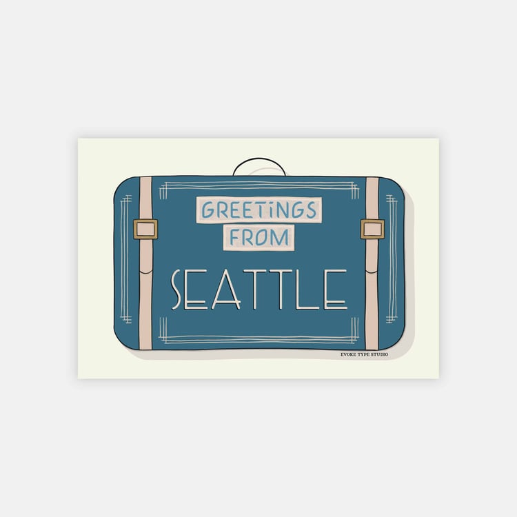 A postcard of a vintage style suitcase with the words “Greetings from Seattle” drawn in unique lettering styles. Artwork has a blue and beige color scheme
