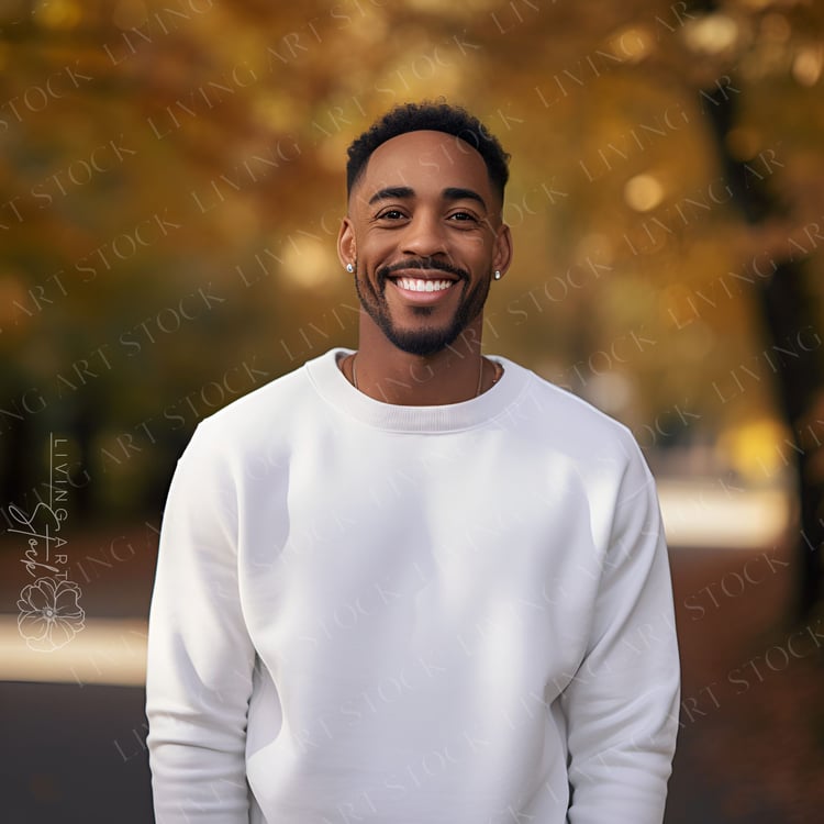 Brown skin black man smiling wearing a blank crewneck sweatshirt and earings in both ears. He is standing in an Autumn outdoor setting.