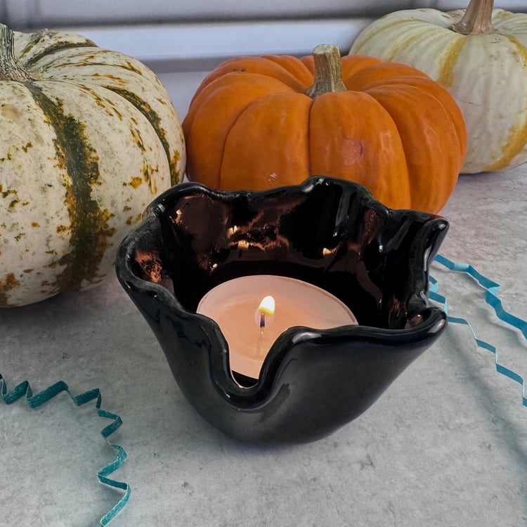 Another angle of a lit black tea light candle on a grey table with pumpkins and blue crinkled paper props.