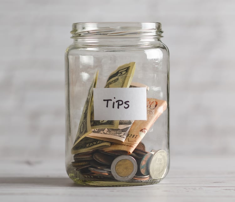 glass jar partially filled with dollar bills and change, label with the word tips on it