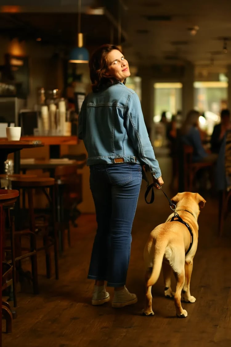 A person leading their unimpressed Yellow Labrador away by its harness, walking out of a coffee shop.