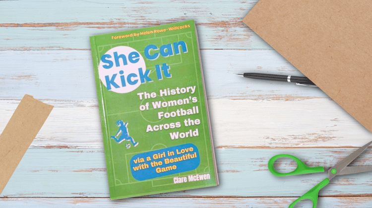 Flat lay of the book “She Can Kick It” on a wooden table with brown wrapping paper, scissors, tape, and a pen — styled like a signed gift ready to wrap.