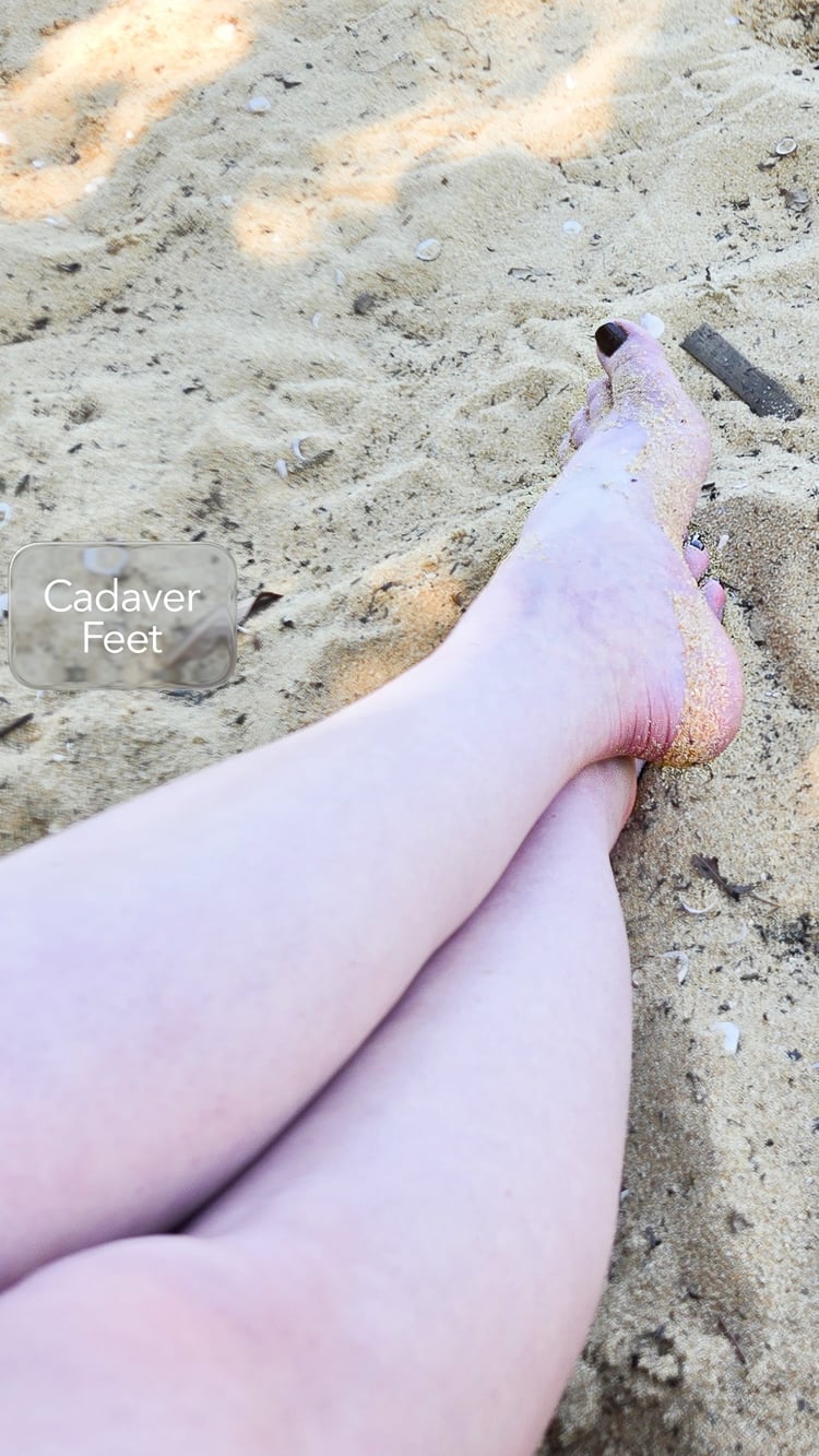 pale feet with dark toe nails resting on a sandy beach