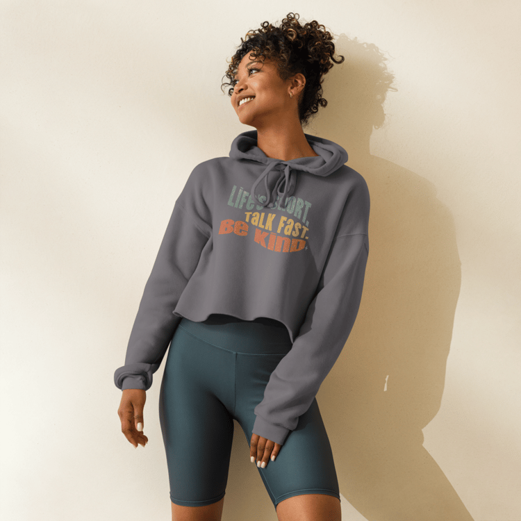 Woman wearing Charcoal cropped hoodie with retro text that reads “Life’s Short. Talk Fast. Be Kind.”