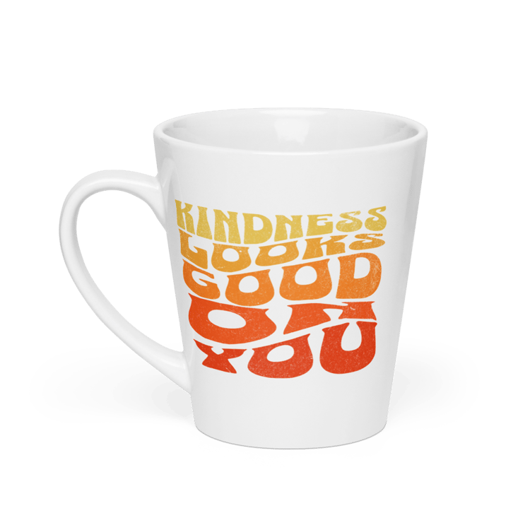 White ceramic latte mug with retro text that reads “Kindness Looks Good On You.”