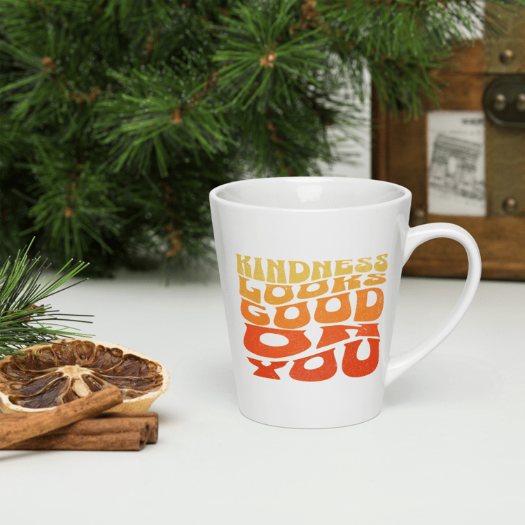 White ceramic latte mug with retro text that reads “Kindness Looks Good On You.”
