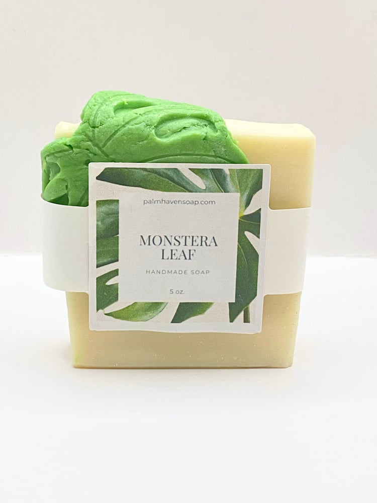 Handmade white soap draped with a green soap monstera leaf
