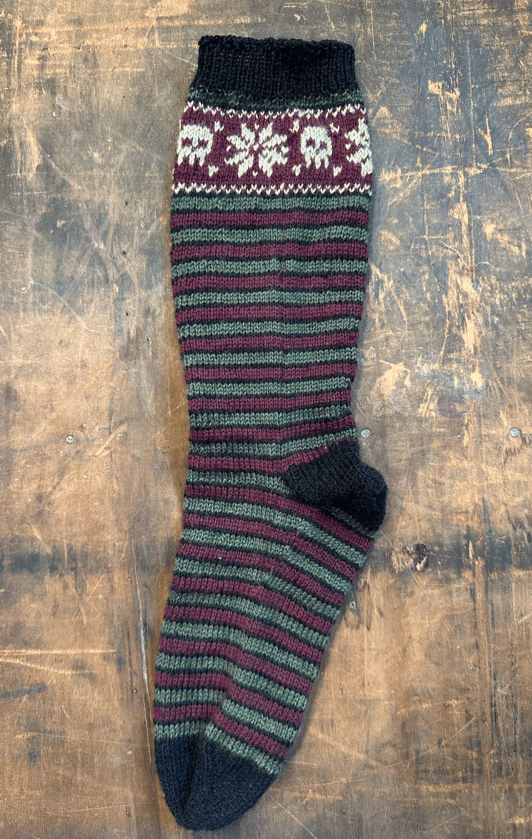 knitted sock with a christmas pattern of stripes and an upper band with a colorwork design.