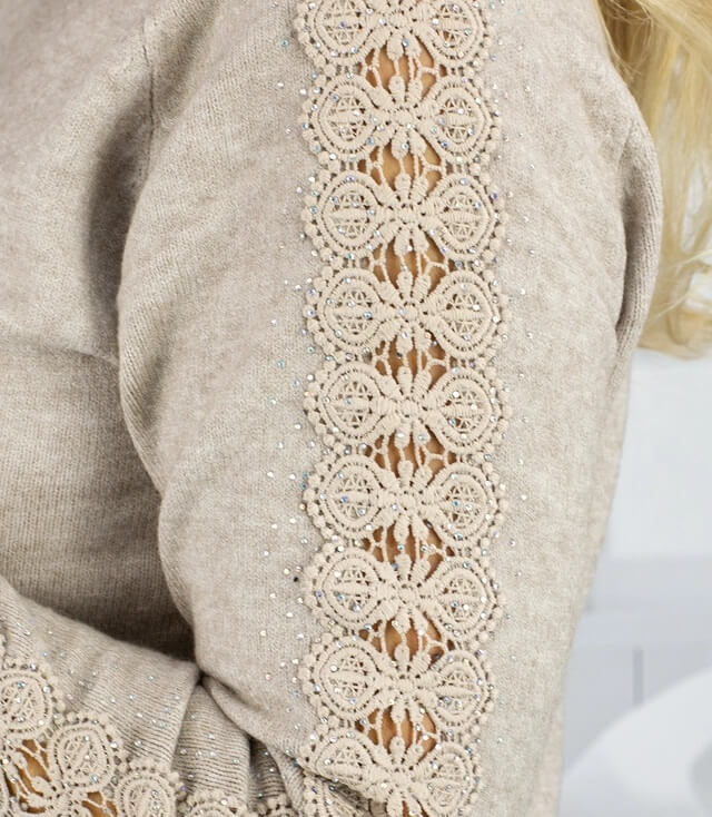 Detailansicht des gestrickten Pullovers mit Spitzenverzierung und glitzernden Akzenten an den Ärmeln.