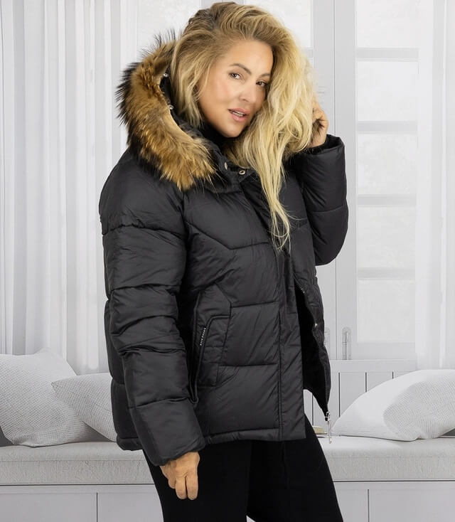 Schwarze Winterjacke mit Kapuze und Fellbesatz, auf einer Person in einem hellen Raum präsentiert.