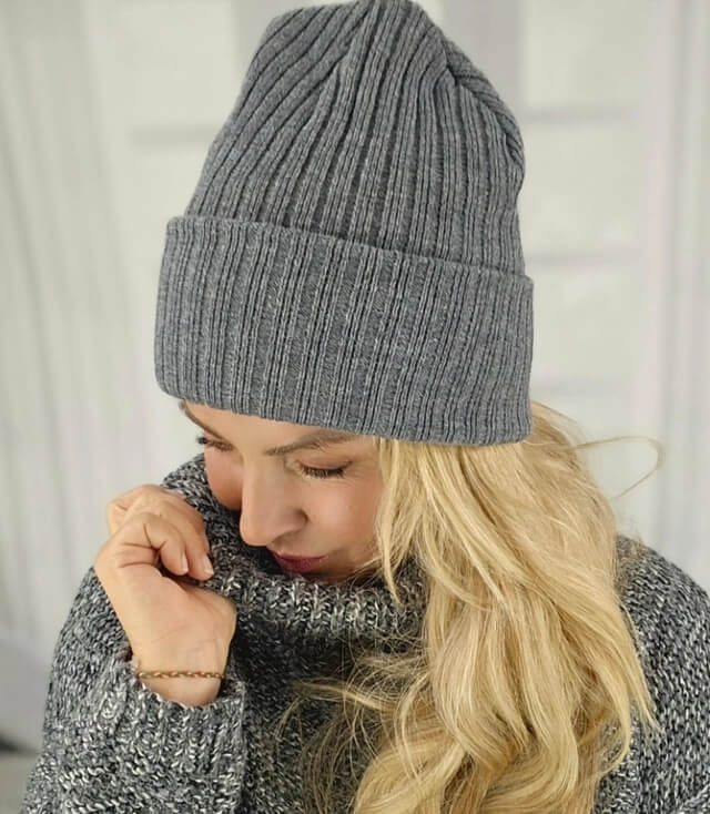 Stylische graue Strickmütze auf einer Frau mit langen blonden Haaren und einem grauen Pullover.
