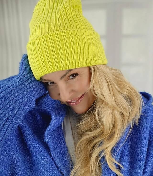 Model trägt eine leuchtend gelbe Mütze und eine blaue Strickjacke mit einem freundlichen Lächeln.
