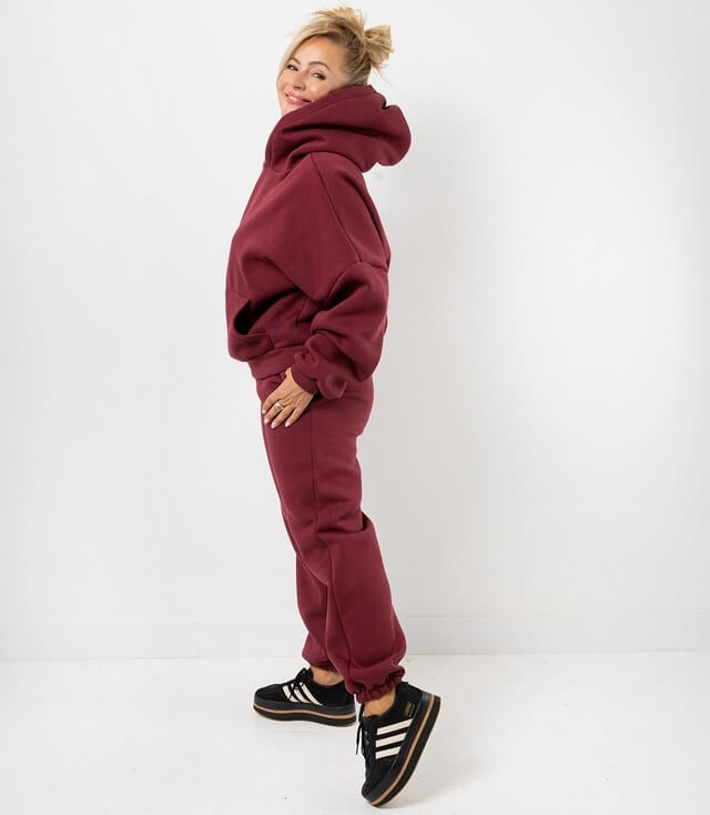 Schicke Frau in bordeauxfarbigem Hoodie und Jogginghose in lässigem Look mit schwarzen Sneakers.