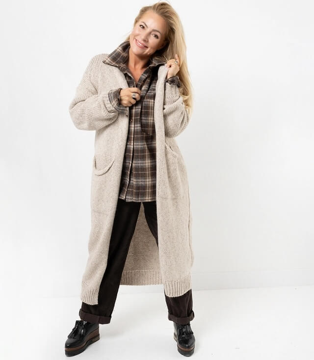 Modischer, langer Cardigan in Beige, getragen von einer Frau mit blauer Jeans und schwarzem Oberteil.