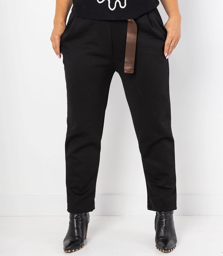 Schwarze Hose mit braunem Gürtel, schmalem Schnitt und hohen Stiefeln kombiniert.