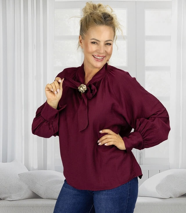 Festliche oversized Bluse in dunkelrot mit goldener Brosche, elegant und modisch kombiniert.