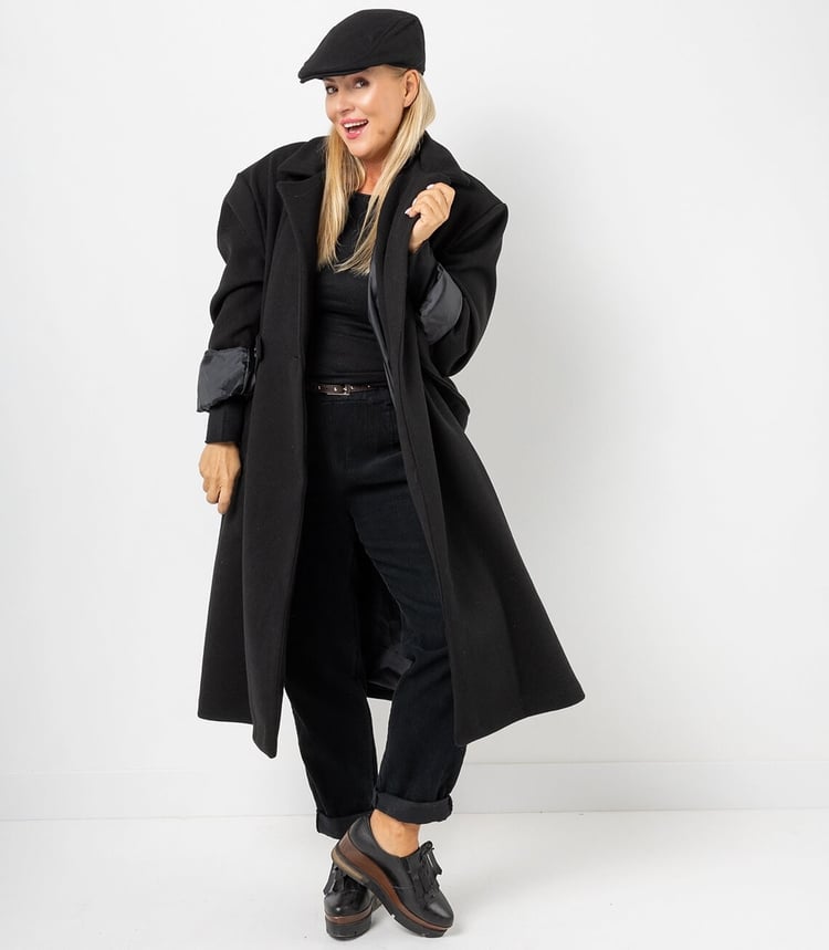 Damen Oversize Trenchcoat großer, offener Kragen und ein kontrastierendes Satinfutter,  in schwarz, lässig getragen mit Cap, lockerer Passform und elegantem Look.