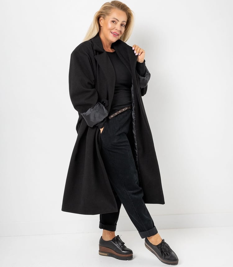 Damen Mantel in Schwarz mit Schulterlinie „Drop Shoulder“ , elegant über schwarzem Outfit, kombiniert mit schwarzen Schuhen.
