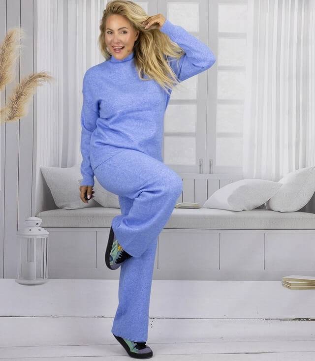 Frau in blauer, kuscheliger Sweatsuit-Kombination mit hoher Taille und lässigem Schnitt, posiert vor einem hellen Hintergrund.