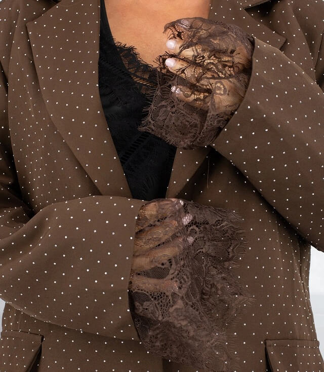Braune Blazerjacke mit weißen Pailetten und eleganten Spitzenärmeln in Detailansicht.