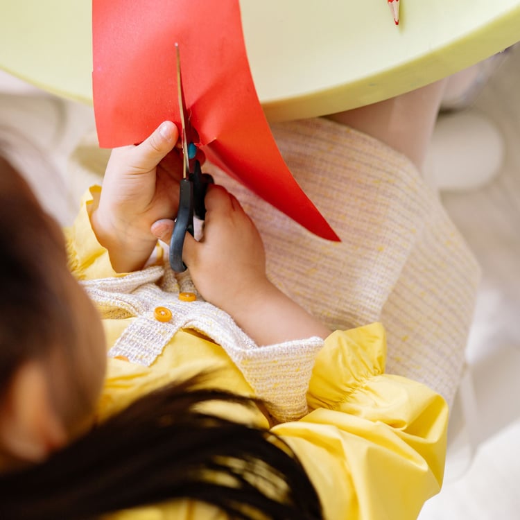 Preschool child practicing fine motor skills and bilateral coordination by cutting paper with child-safe scissors.