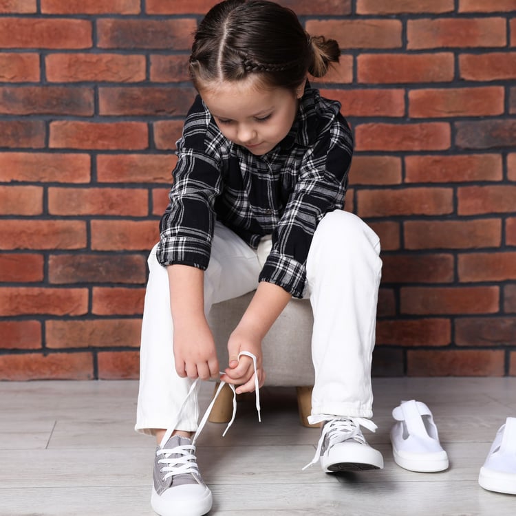 Child practicing bilateral coordination by tying shoelaces, a key self-care skill for preschoolers.