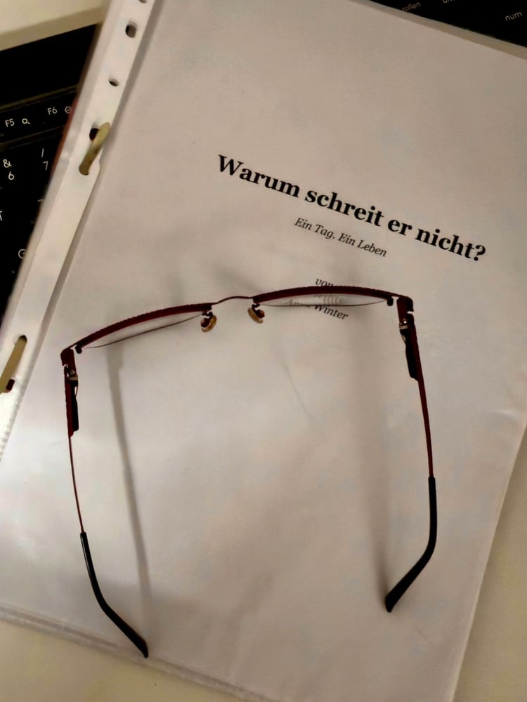 Manuskript „Warum schreit er nicht? – Ein Tag. Ein Leben.“ mit Brille auf weißem Hintergrund