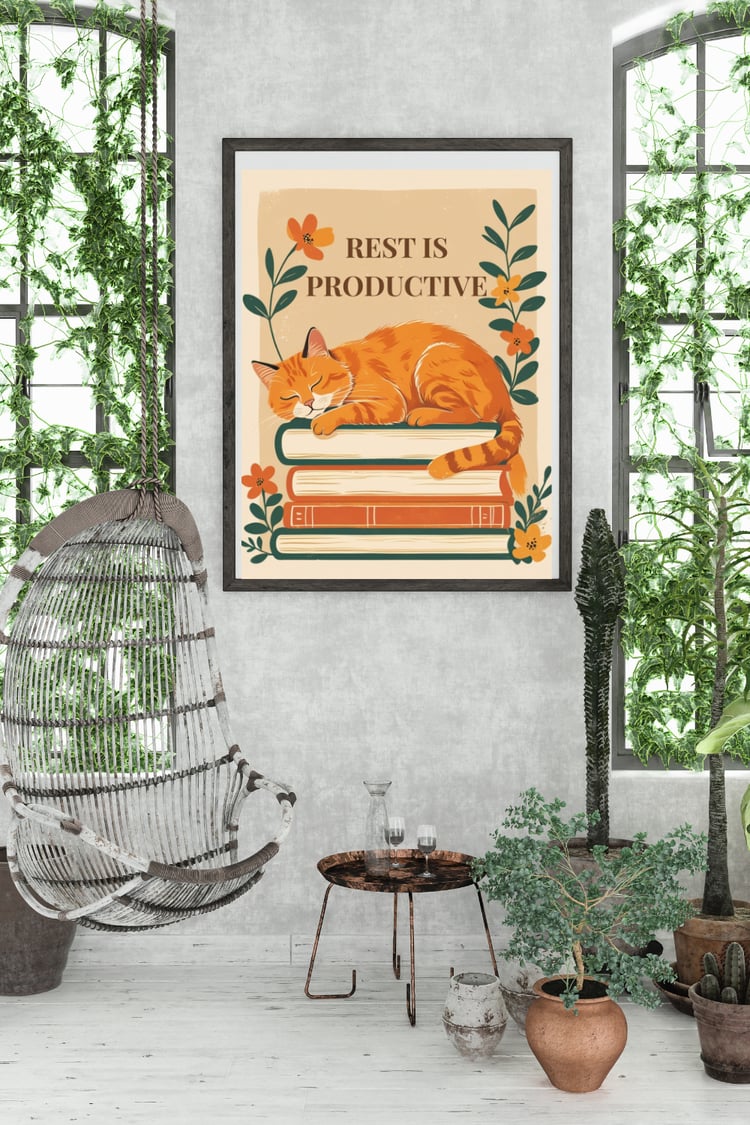 Rest is productive cat wall art print in black frame on concrete wall in bohemian living room with hanging plants, rattan hammock chair, terracotta pots, and natural sunlight - vintage printable poster for book lovers
