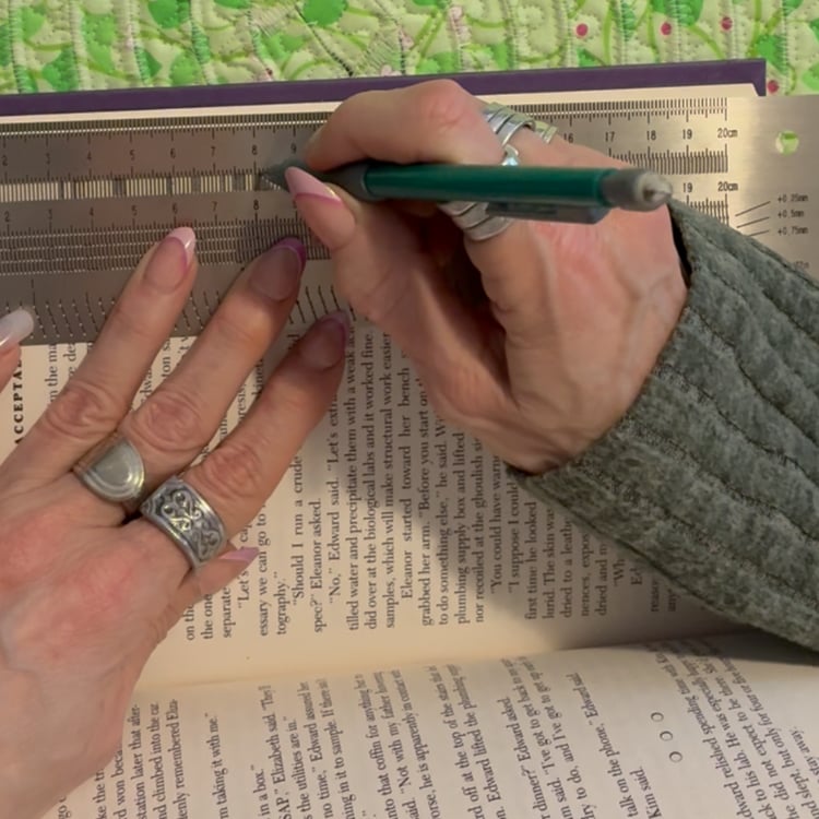 Close-up of hands marking pages of a book with a ruler and pencil for a book folding project, demonstrating precise measurement and original folded book art design in the Narnation creative studio.