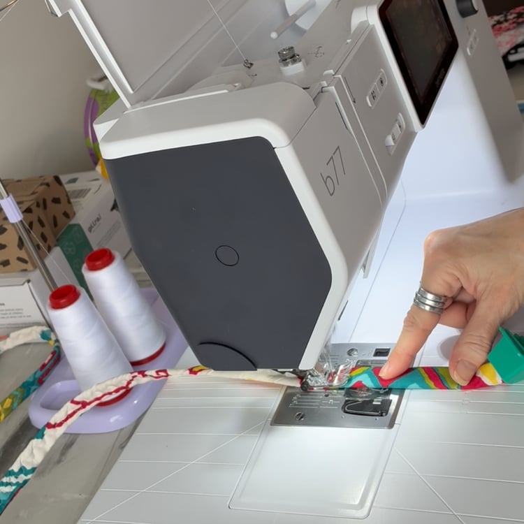 Close-up of a sewing machine stitching a cord for a jelly roll rug, showing hands guiding fabric and the machine in action, demonstrating upcycled sewing techniques and creative textile projects in a Narnation studio setup.