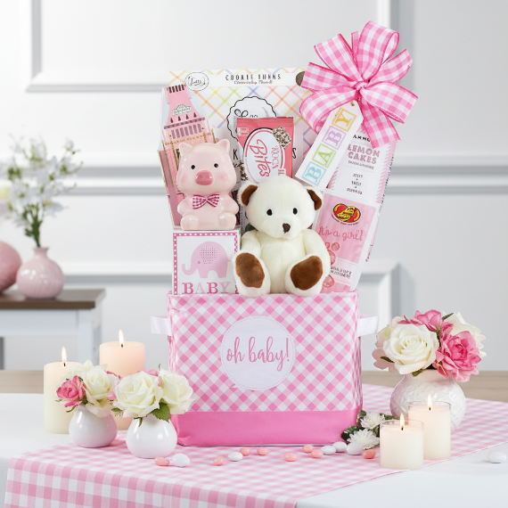 Pink baby gift basket with teddy bears, cookies, and flowers on a checkered tablecloth.