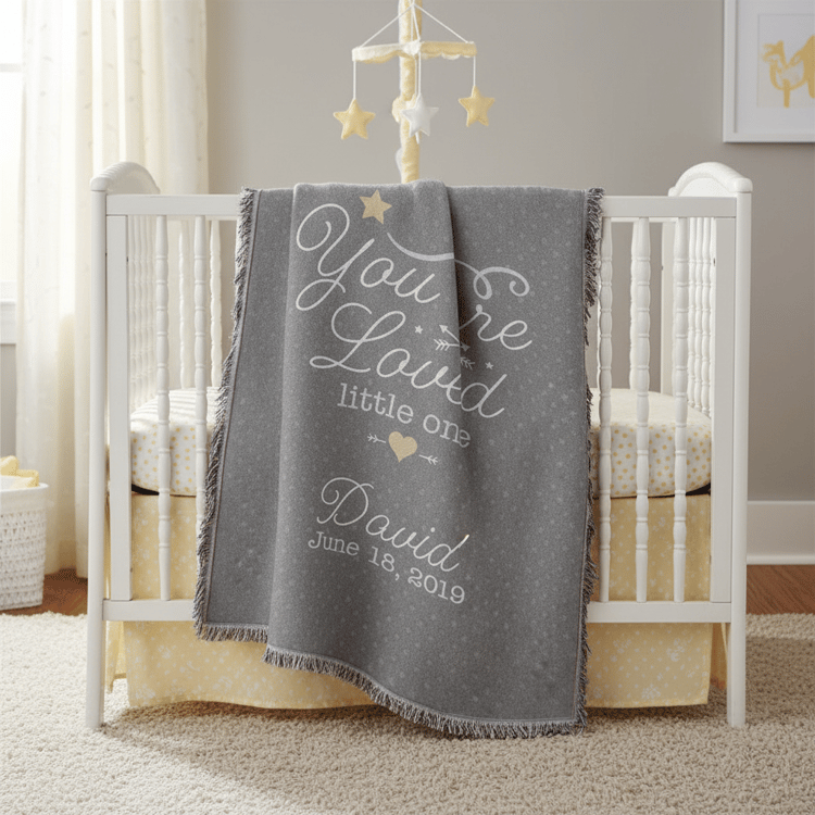Gray blanket with personalized text over a crib in a nursery