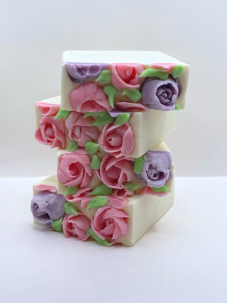 stack of handmade white soaps topped with handmade pink and lavender soap flowers