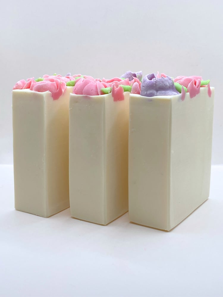 three white soaps topped with handmade pink and lavender roses