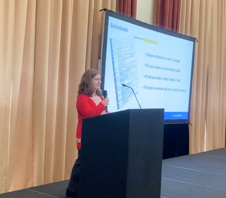 person presenting at a work conference from a lectern with an information slide behind them