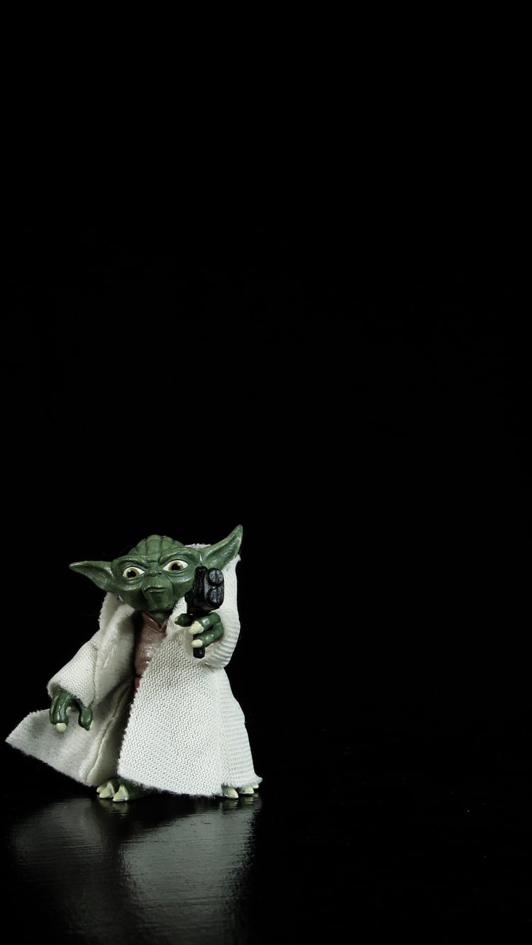 Yoda action figure on a black  background. He is pointing a blaster at the viewer.