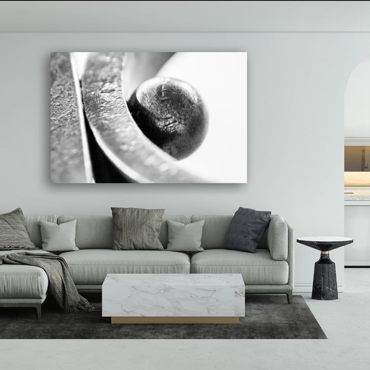 A large horizontal print of an abstract black and white steel macro photograph hangs on a light gray wall above a modern gray sectional sofa in an upscale living room.