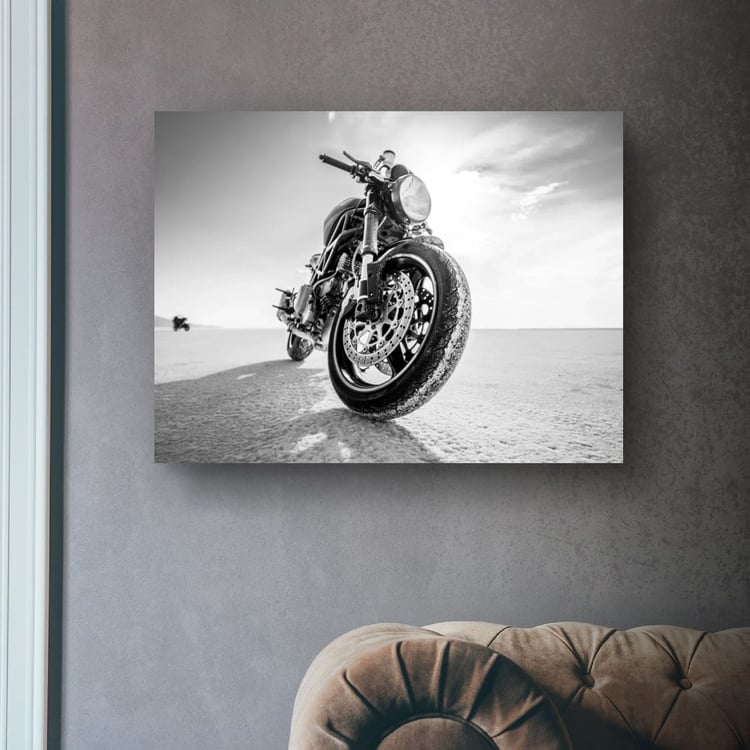 A large horizontal  print of a black and white motorcycle on the salt flats hangs on a dark textured concrete wall centered above a plush, brown tufted leather sofa.