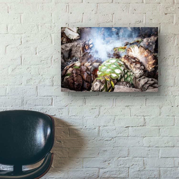 A large horizontal print of a mezcal agave roasting scene hangs on a painted white brick wall above a black leather office chair.