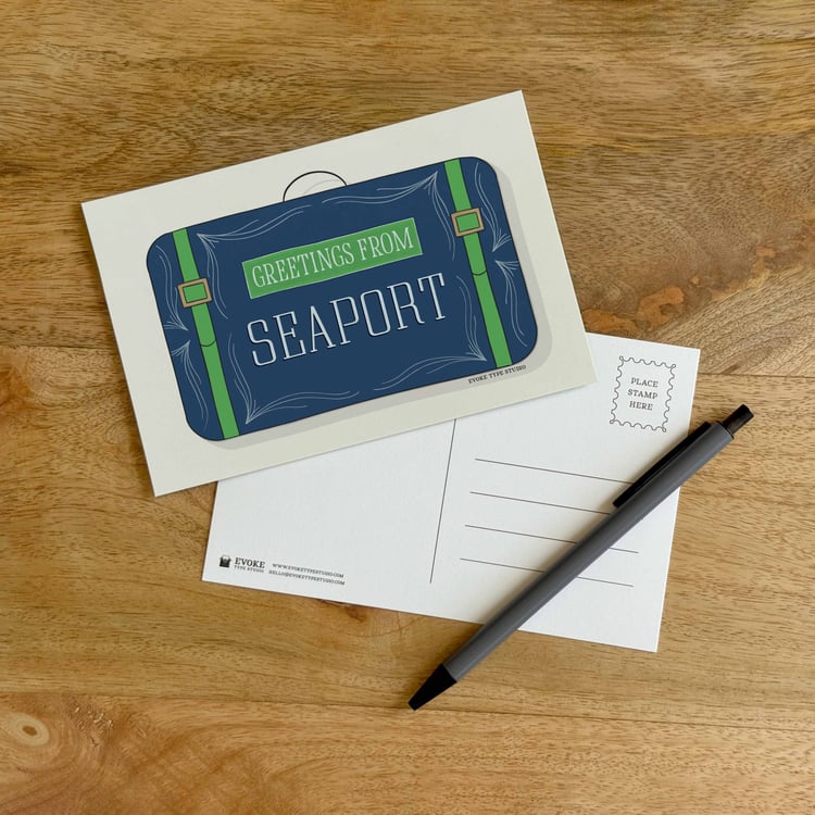 The front and back sides of a postcard with a pen placed on top. The front features a vintage suitcase illustration and the back shows the address lines and stamp indicator.