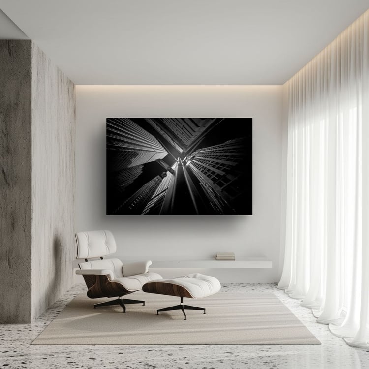 A large frameless canvas print of a black and white abstract skyscraper photograph hangs on a white wall in a luxury minimalist room featuring a white leather lounge chair and ottoman.