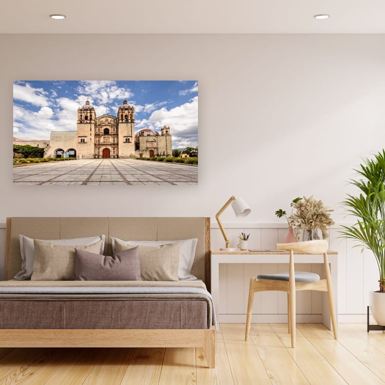 large canvas print of the empty Santo Domingo church in Oaxaca hangs on a clean white wall above a modern wooden bed frame and minimalist writing desk.