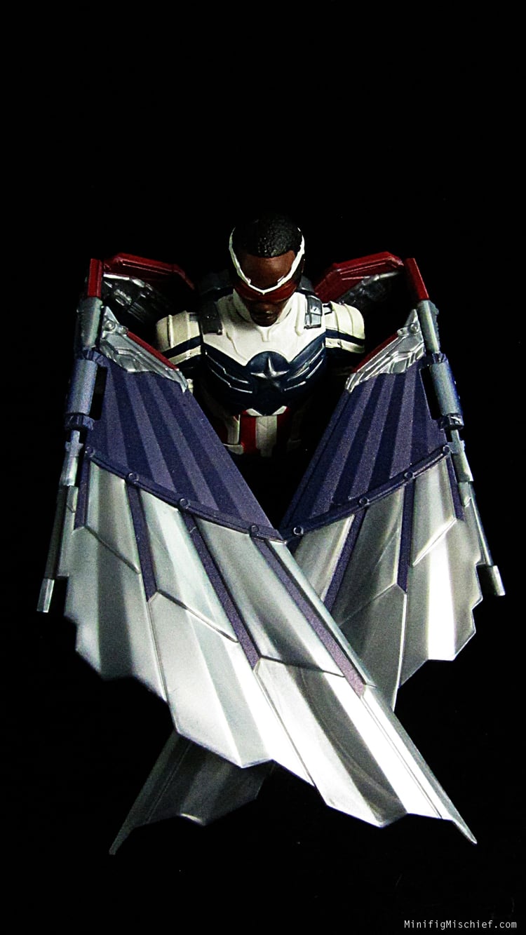 pic of sam wilson action figure. his wings are folded in front of him and his head is bowed. hes in front of a black background.