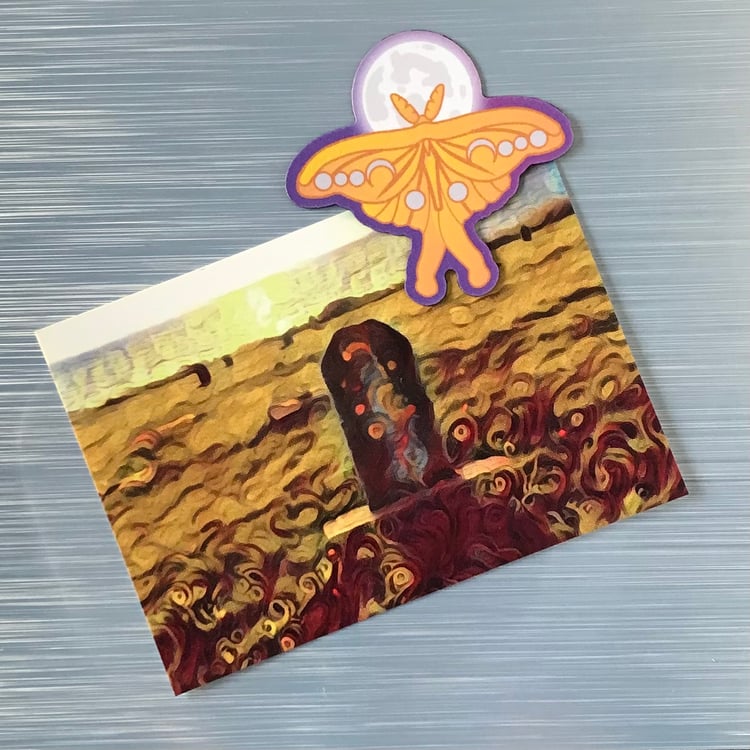 A luna moth and moon fridge magnet shown in use holding up a postcard.