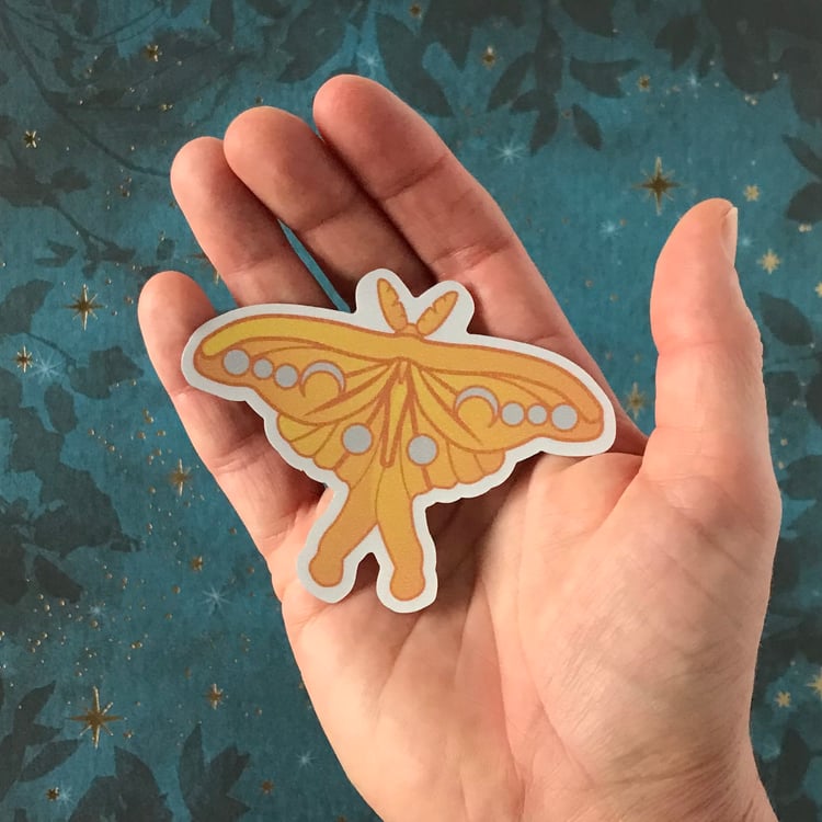 A luna moth vinyl decal shown in-hand for scale.