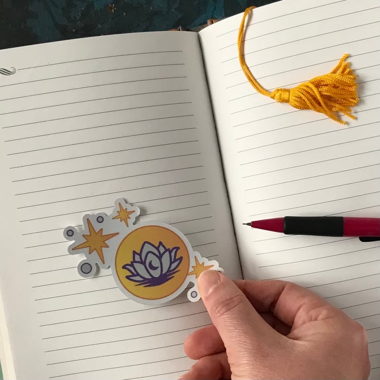 A lotus and moon-themed decal being placed onto a personal journal page.