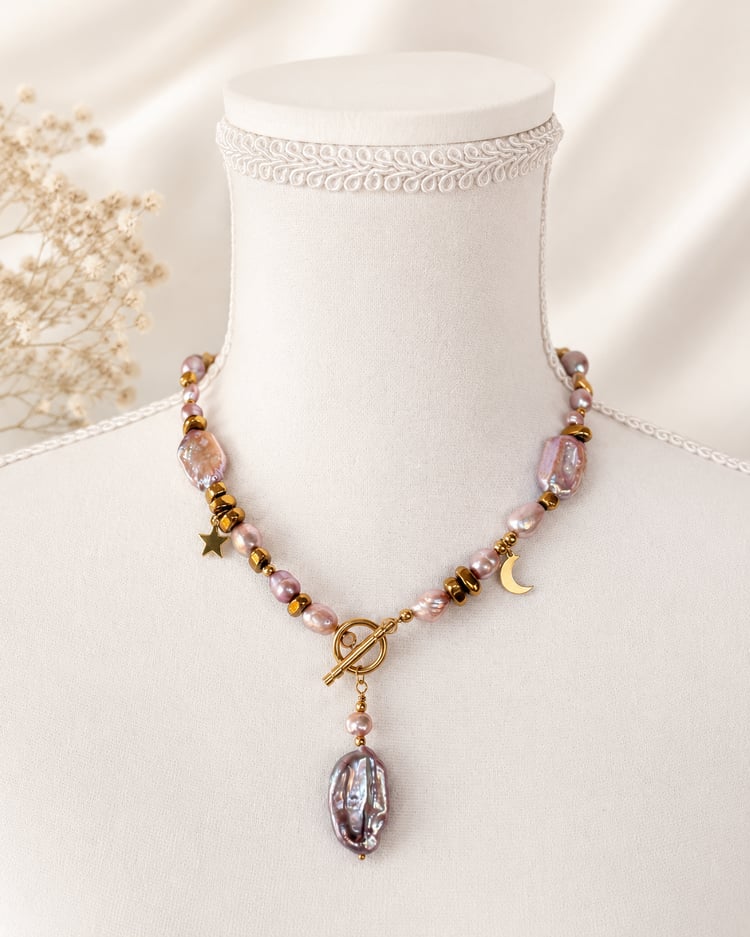 Collana artigianale con perle d’acqua dolce rosa, perla barocca, ematite dorata e chiusura T-Bar su manichino beige.