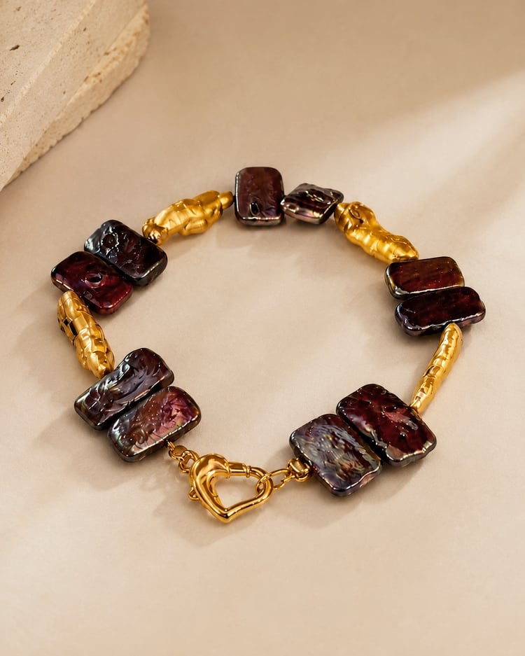 Bracciale artigianale con perle d’acqua dolce e chiusura a cuore in acciaio inox su sfondo beige.