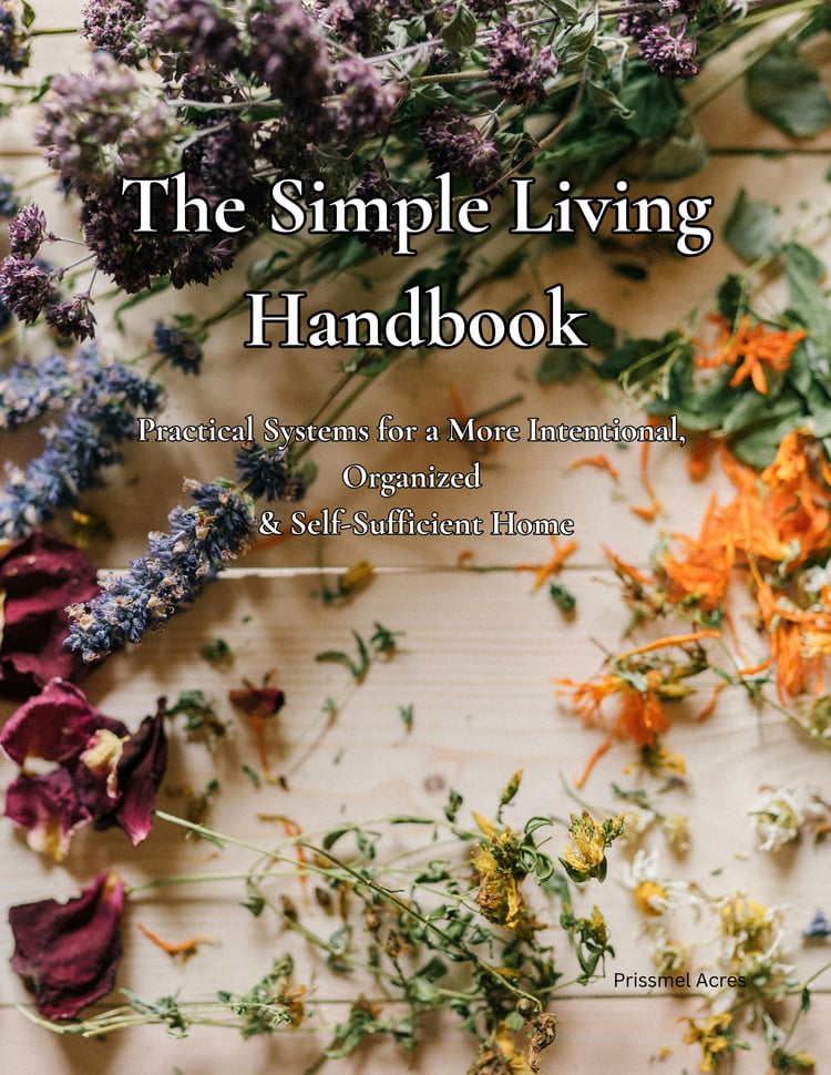 Fresh medicinal herb cuttings arranged on a rustic wooden table beside The Simple Living Handbook 151-page printable PDF guide featuring intentional living, traditional skills, homemaking, and simple living resources.