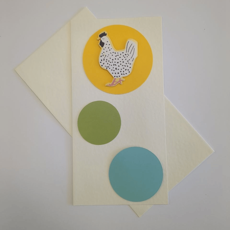 A tall portrait card in cream with a matching cream envelope. Three circles bubble up the card in different colours and sizes. The bottom circle is turquoise blue, the middle one is smaller and green. The top circle has a motif of a white chicken with bla